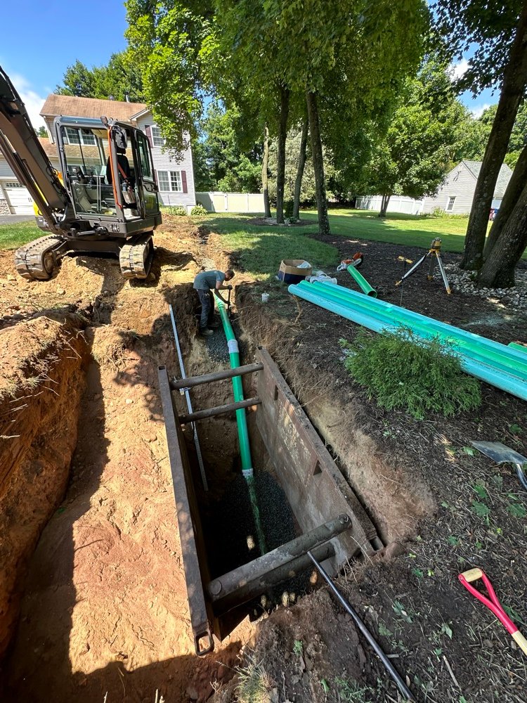 Shored sewer line excavation trench next to a home
